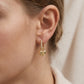 Close-up view of a model wearing gold beaded moissanite huggie hoop earrings with puffed heart lock charm.