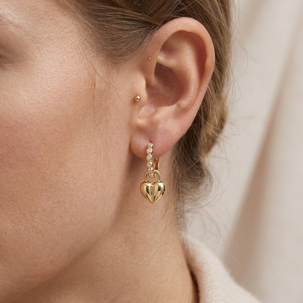 Close-up view of a model wearing gold beaded moissanite huggie hoop earrings with puffed heart lock charm.