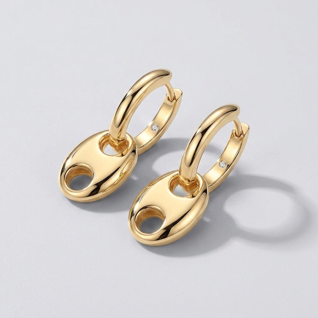 Pair of gold mariner anchor link dangle huggie hoop earrings on a light gray background.