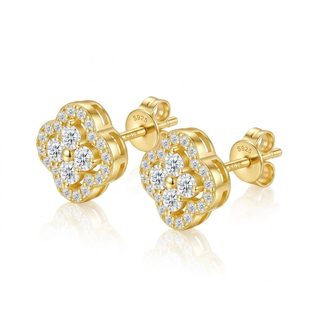 Pair of gold round cut moissanite four-leaf clover cluster stud earrings with pave halo on a gray surface.