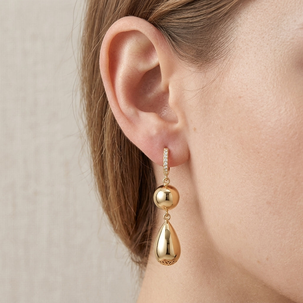 Close-up view of a model wearing gold sphere teardrop moissanite dangle hoop earrings.