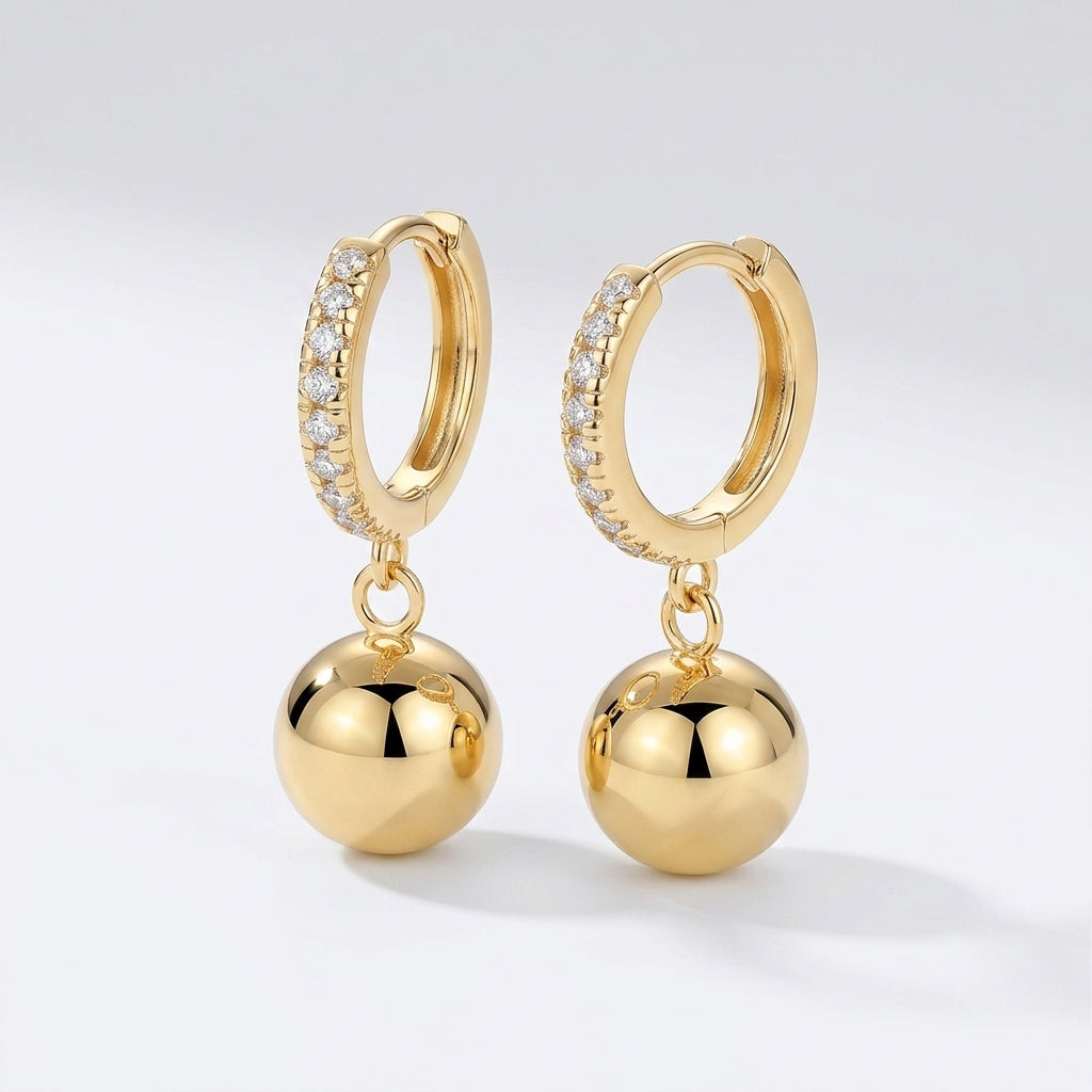 Pair of gold spherical bead drop moissanite huggie hoop earrings with reflective finish.