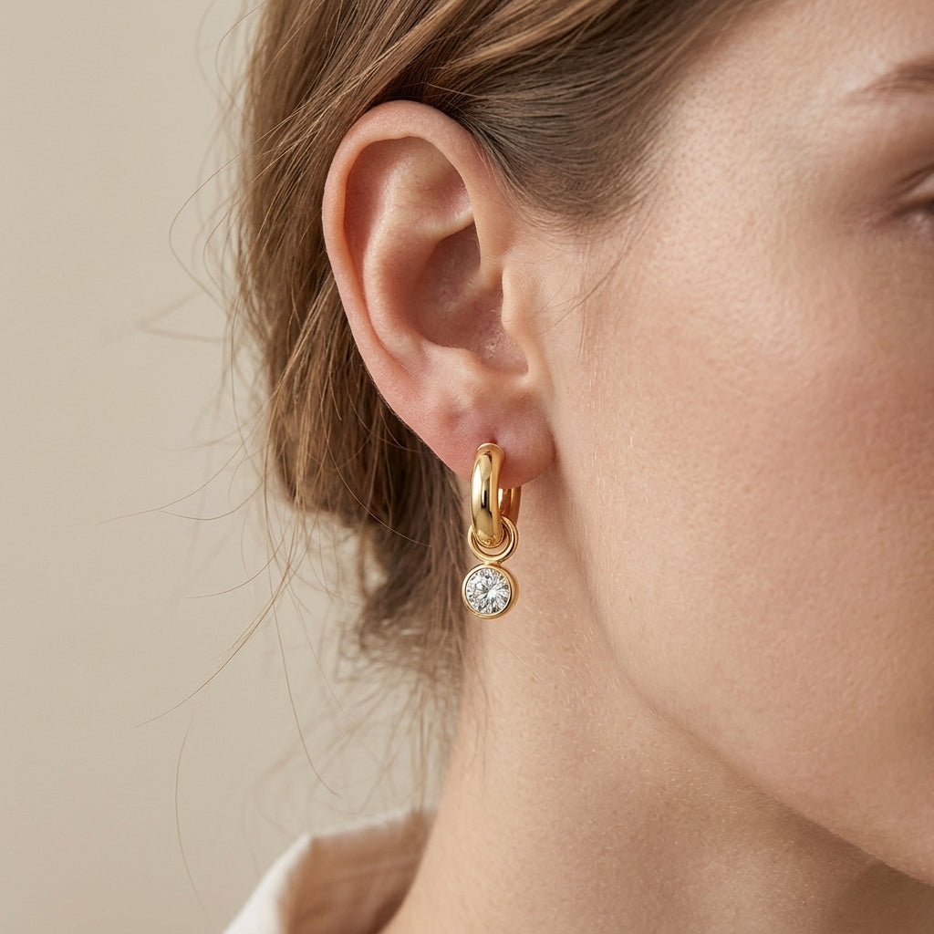 Close-up view of a model wearing classic gold tubular hoop earrings with round moissanite drop charm.