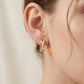 Close-up view of a model wearing the gold crisscross X moissanite huggie hoop earrings.