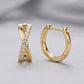 Gold X-shaped huggie earrings with pavé moissanite displayed on a gray background.