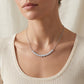 Model wearing graduated bezel set moissanite curved smile necklace on collarbone.