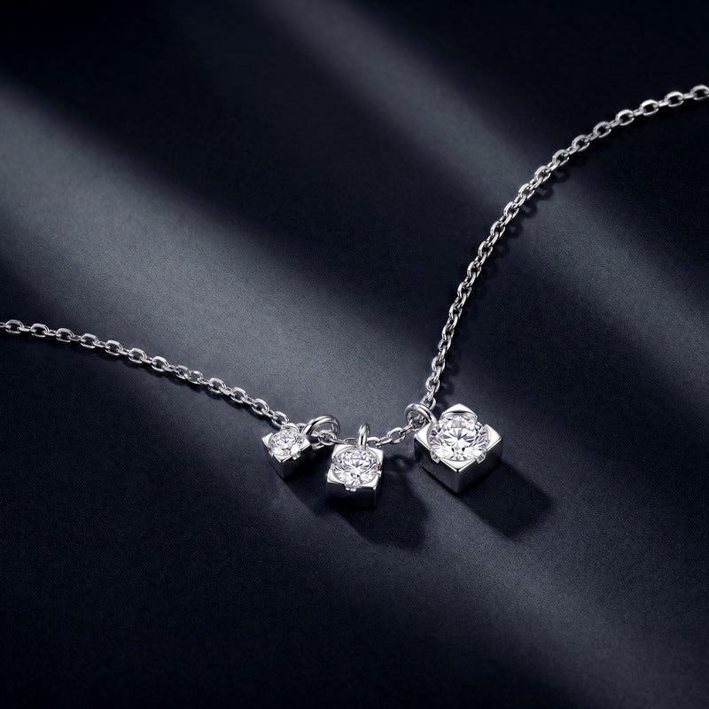 Graduated moissanite trio square drop necklace on dark blue silk background.
