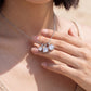Close-up shot of model hand touching graduated moissanite trio square drop pendant by the beach.