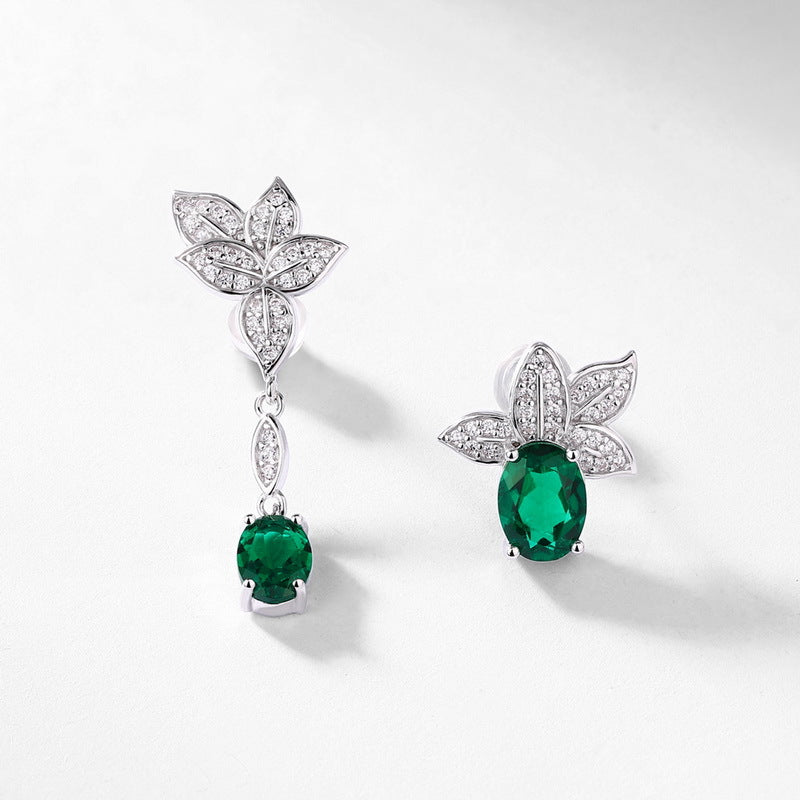 Diagonal studio shot of handcrafted emerald botanical mismatched earrings casting a soft gradient shadow.