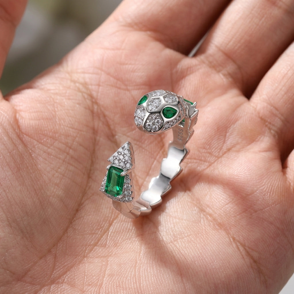 Handheld view in the palm under directional natural light capturing a handcrafted emerald eyes serpent adjustable open ring.