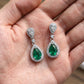 Handheld view in the palm under natural soft light capturing handcrafted lab-grown emerald open halo drop earrings.