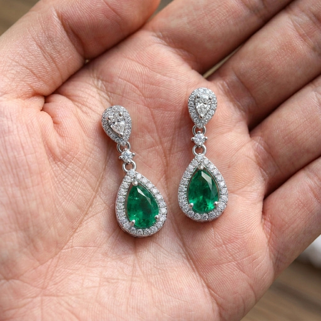 Handheld view in the palm under natural soft light capturing handcrafted lab-grown emerald open halo drop earrings.