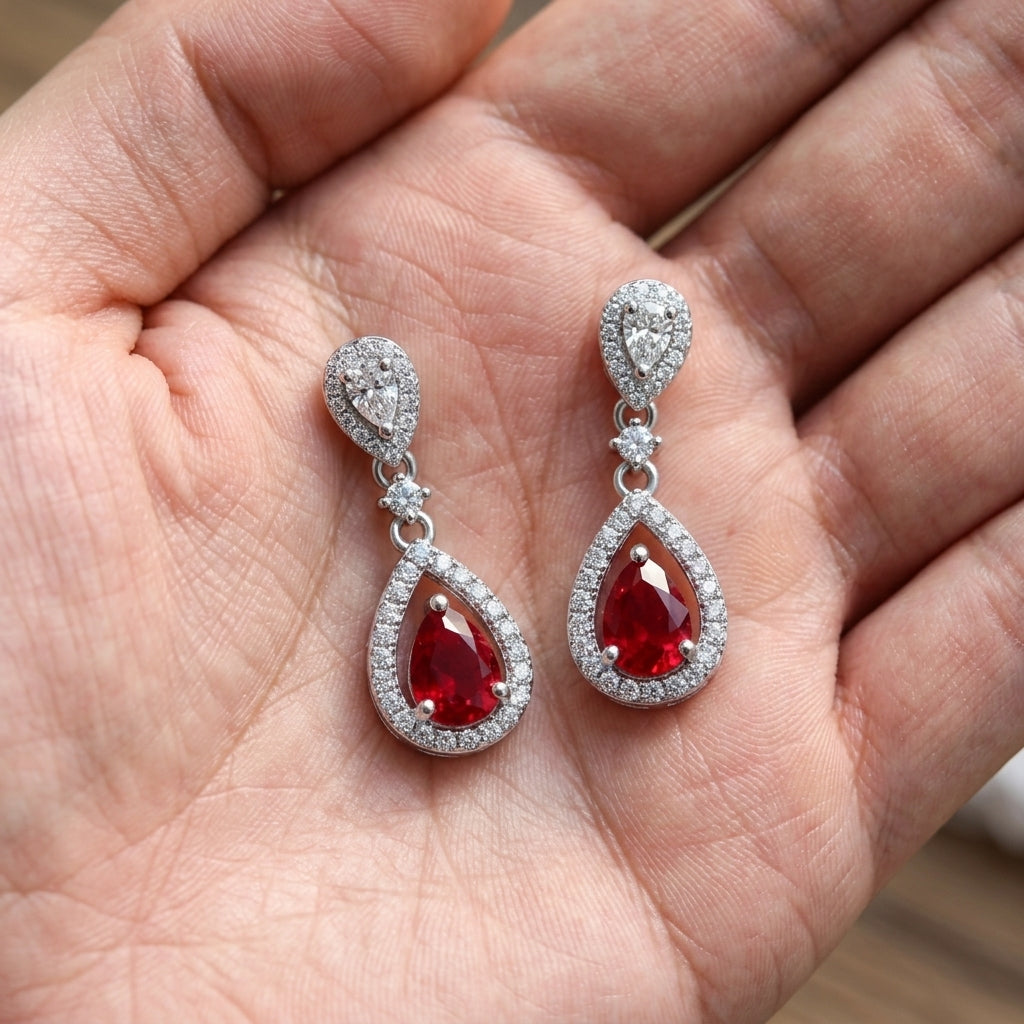 Handheld view in the palm under natural soft light capturing handcrafted lab-grown ruby open halo drop earrings.