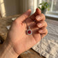Handheld view in the palm under golden-hour natural light capturing a handcrafted lab-grown ruby square pendant.