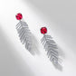 Side angle studio view of square ruby wheat tassel statement earrings resting on a white geometric prop.