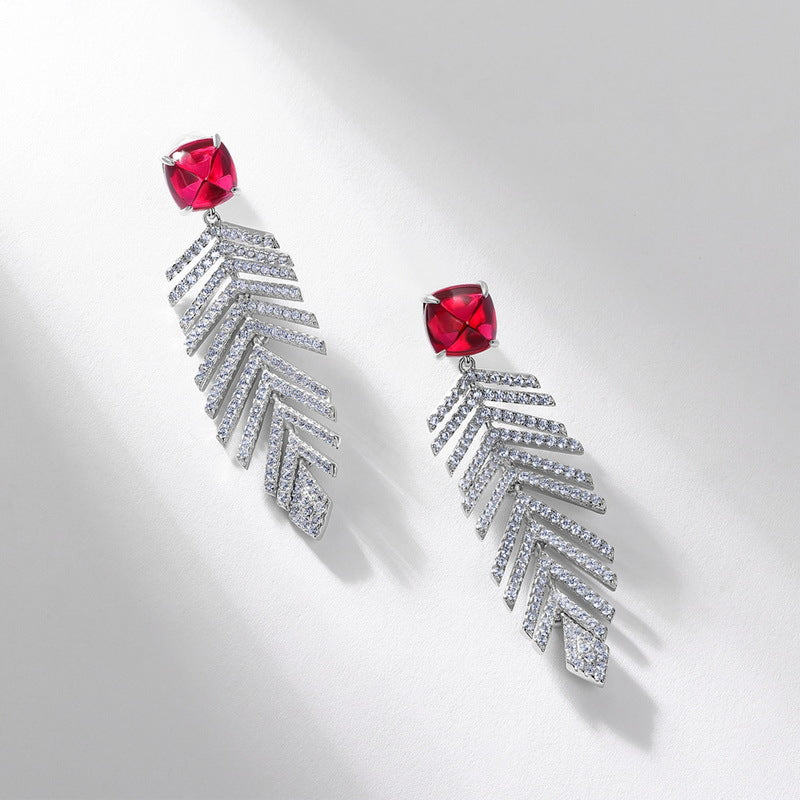Side angle studio view of square ruby wheat tassel statement earrings resting on a white geometric prop.