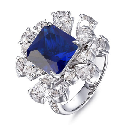 Three-quarter studio shot of a luxury asscher-cut blue sapphire floral cluster statement ring with a polished shank.