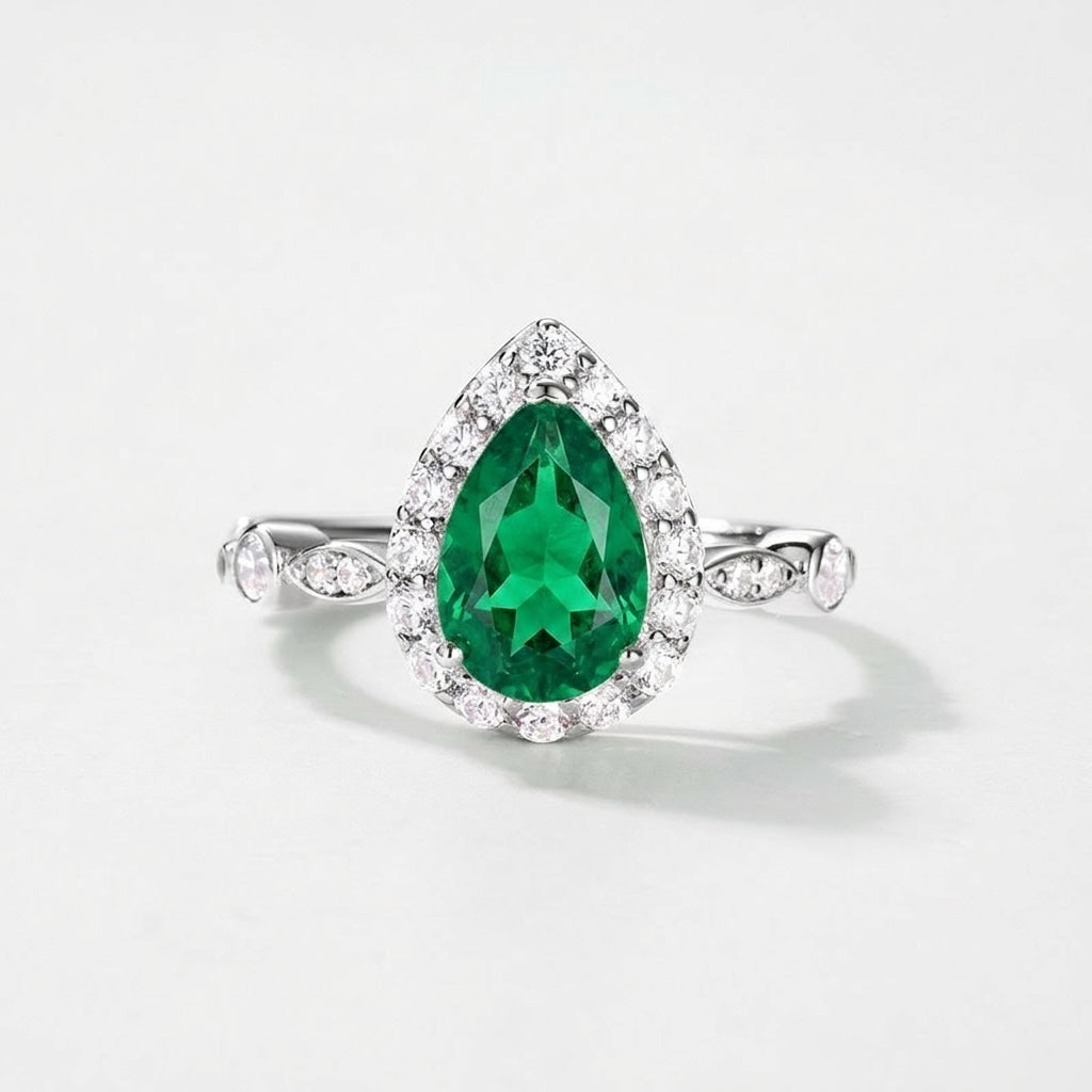 White background front view showcasing a handcrafted pear-cut emerald solitaire halo ring with an Art Deco pave band.