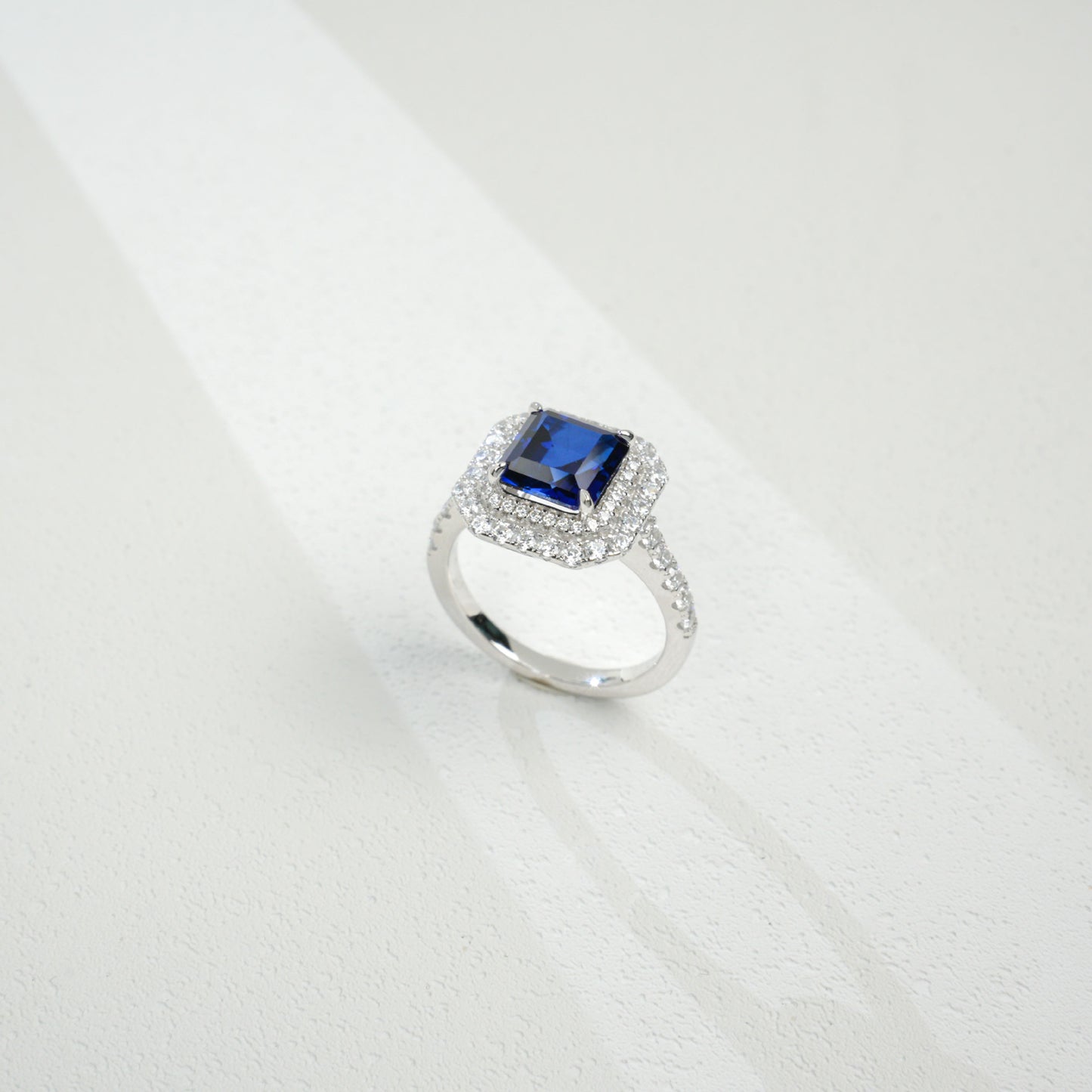 Top-down studio shot showcasing a handcrafted royal blue sapphire double halo cocktail ring casting a gradient shadow.