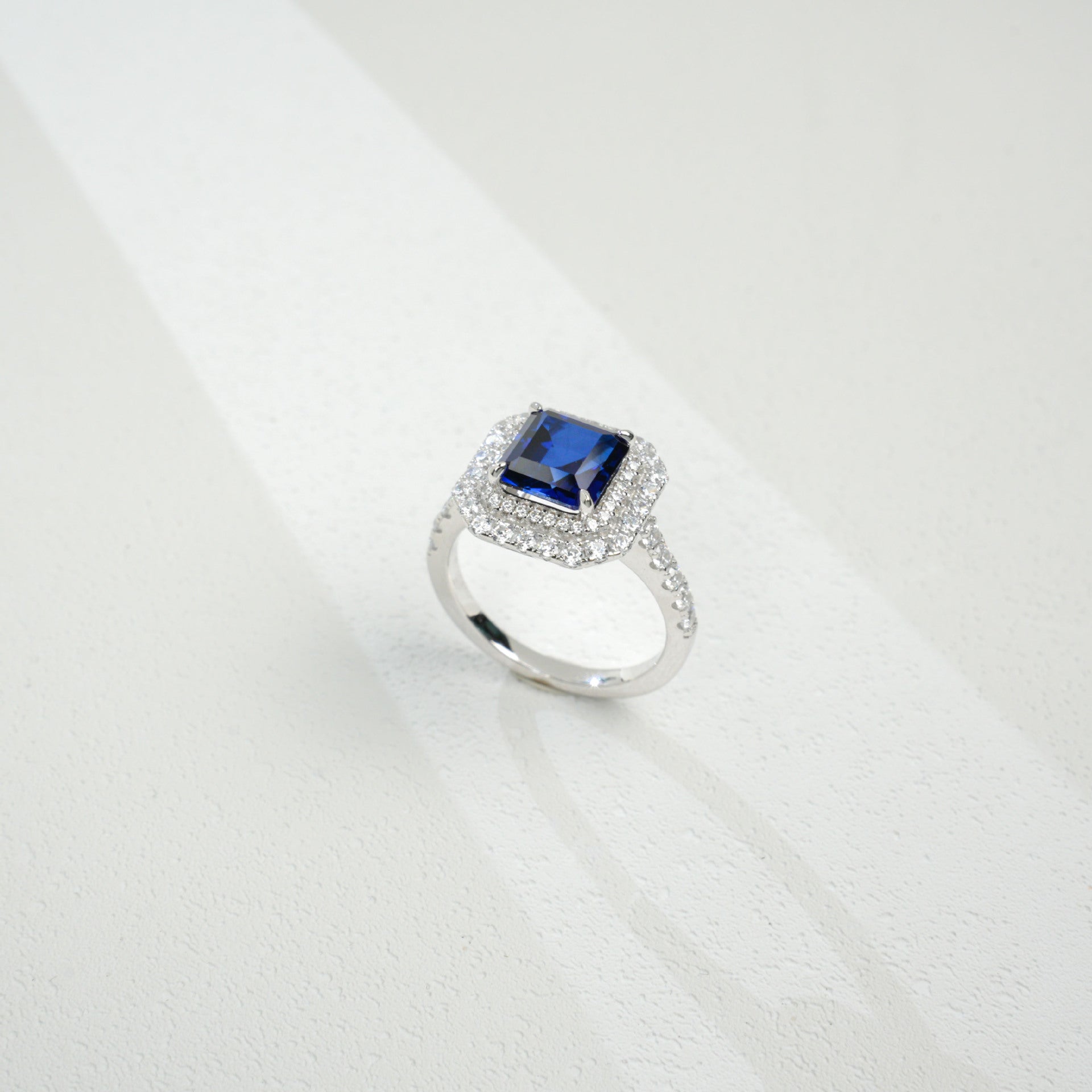 Top-down studio shot showcasing a handcrafted royal blue sapphire double halo cocktail ring casting a gradient shadow.