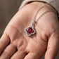 Handheld view in the palm under natural soft light capturing a handcrafted ruby openwork clover pendant necklace.
