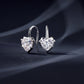 Pair of heart cut moissanite shepherd hook drop earrings displayed on dark textured fabric.