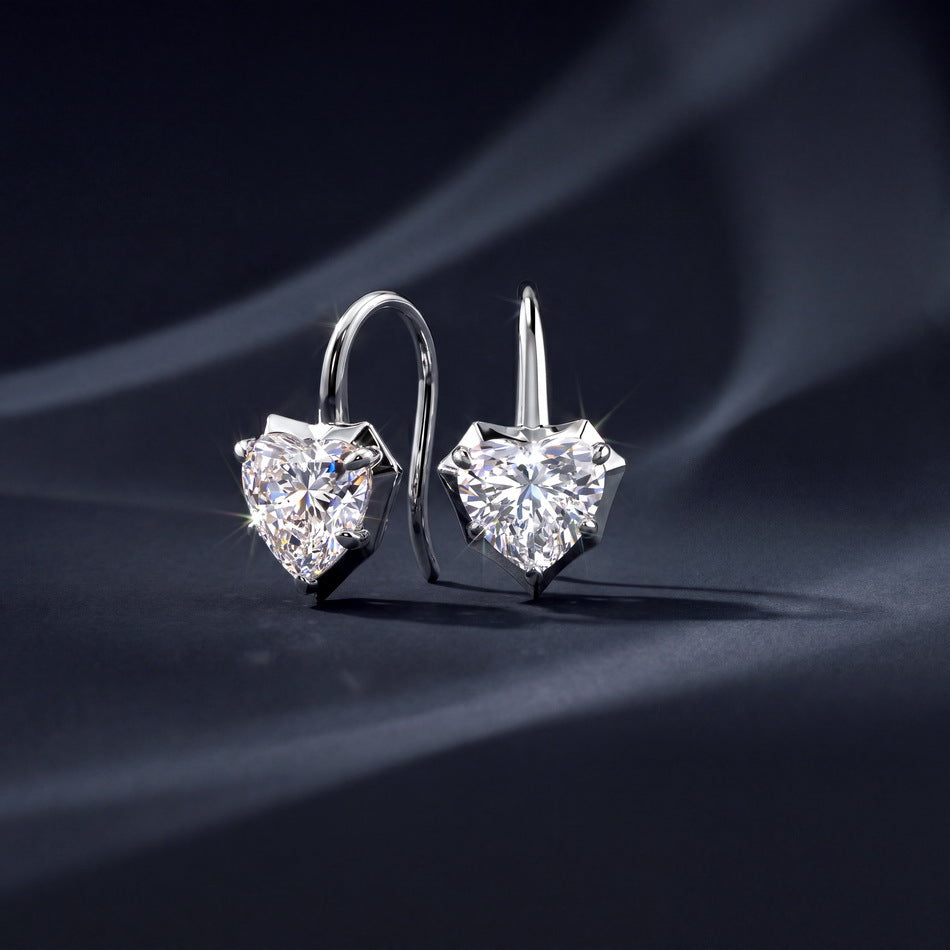 Pair of heart cut moissanite shepherd hook drop earrings displayed on dark textured fabric.