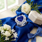 Luxury heart blue sapphire halo ring styled with white flowers and ribbon, old money aesthetic