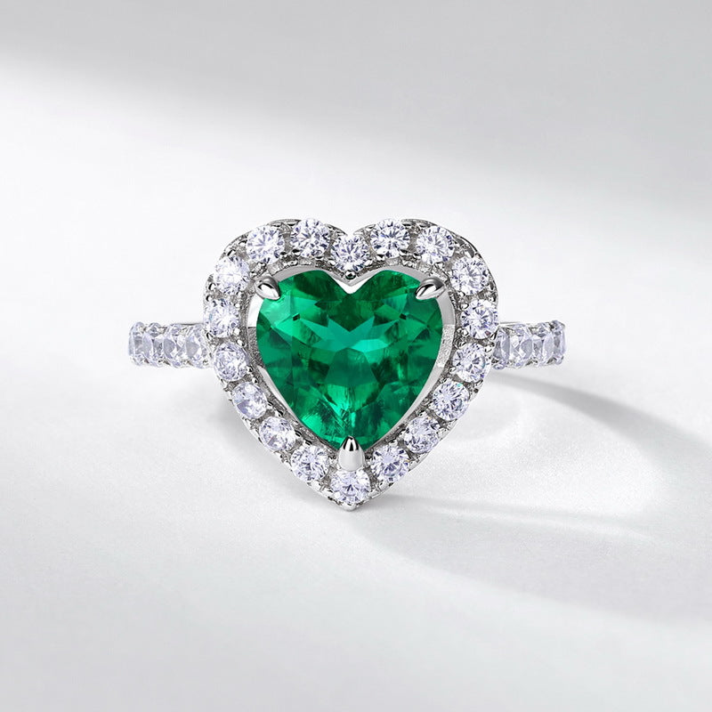 White background product view of an elegant heart-shaped emerald engagement ring in white gold or silver pave band.
