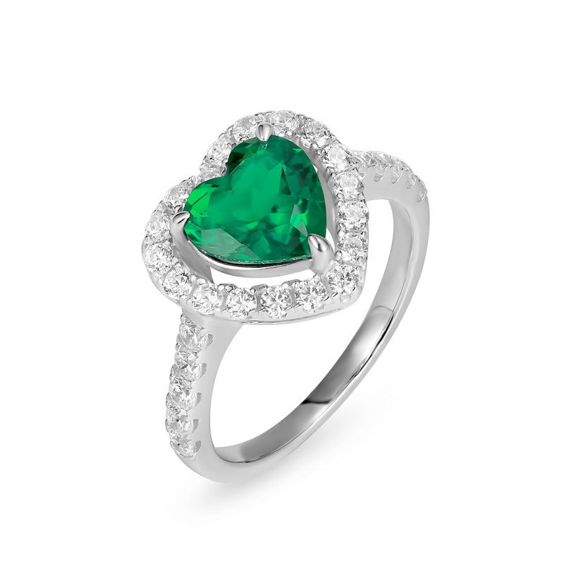 Side angle view of a luxury heart-shaped emerald statement ring on a white surface with soft shadows.