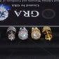 Silver and gold iced out 3D crown cylinder solitaire moissanite stud earrings with pave setting in front of GRA certificate card