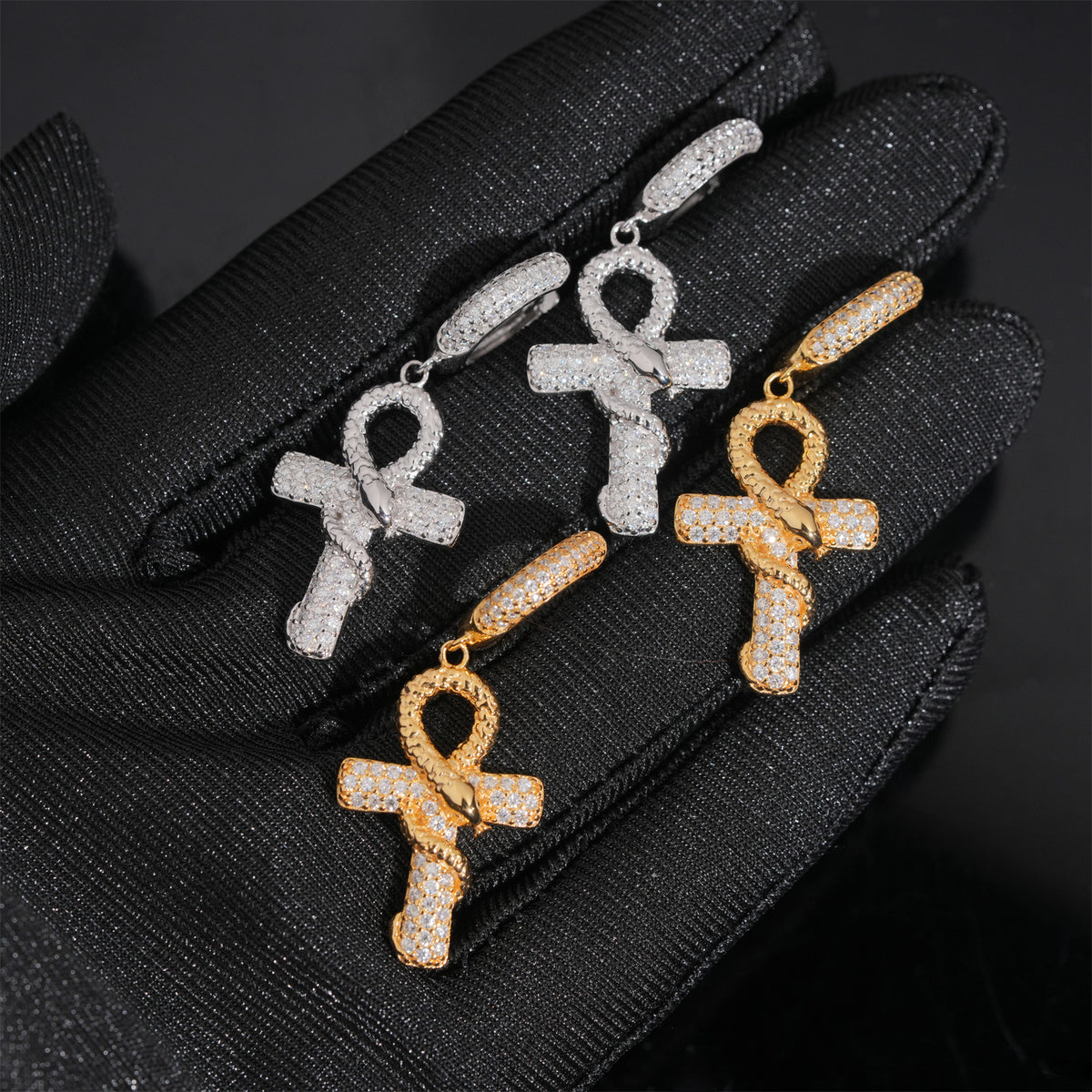 Gold and silver iced out ankh cross snake dangle moissanite earrings on gloved hand showing hinged clasp