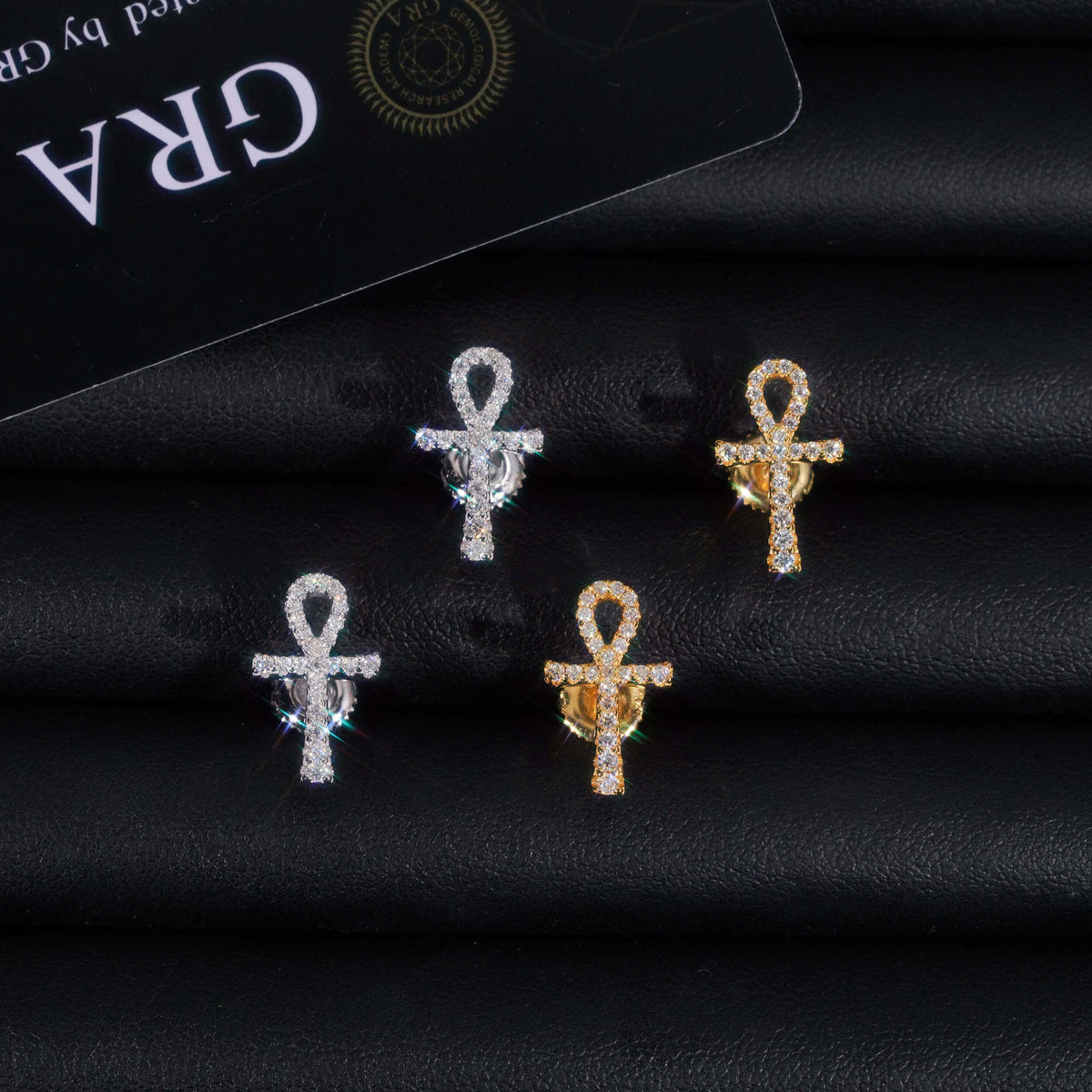 Pair of silver and gold iced out ankh key of life cross moissanite stud earrings on dark leather background