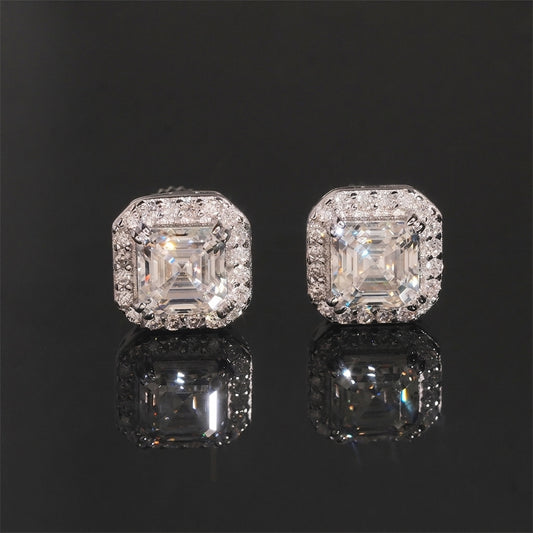 Iced out asscher cut moissanite halo stud earrings in sterling silver resting on dark reflective background