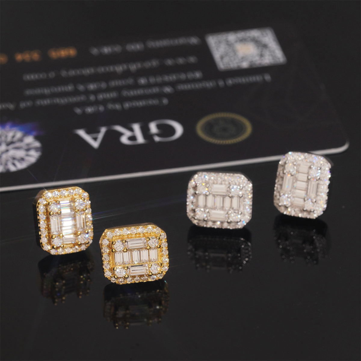 Silver and gold iced out baguette cut halo moissanite stud earrings in front of GRA card