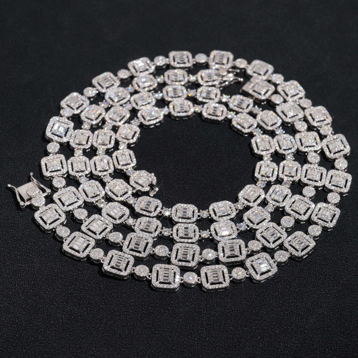 Silver iced out baguette halo and round alternating moissanite tennis chain coiled on dark surface