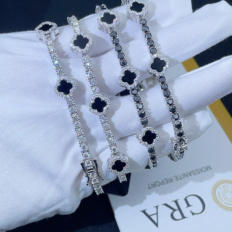 Gloved hand holding iced out black enamel clover tennis chain moissanite bracelets with double safety box clasp