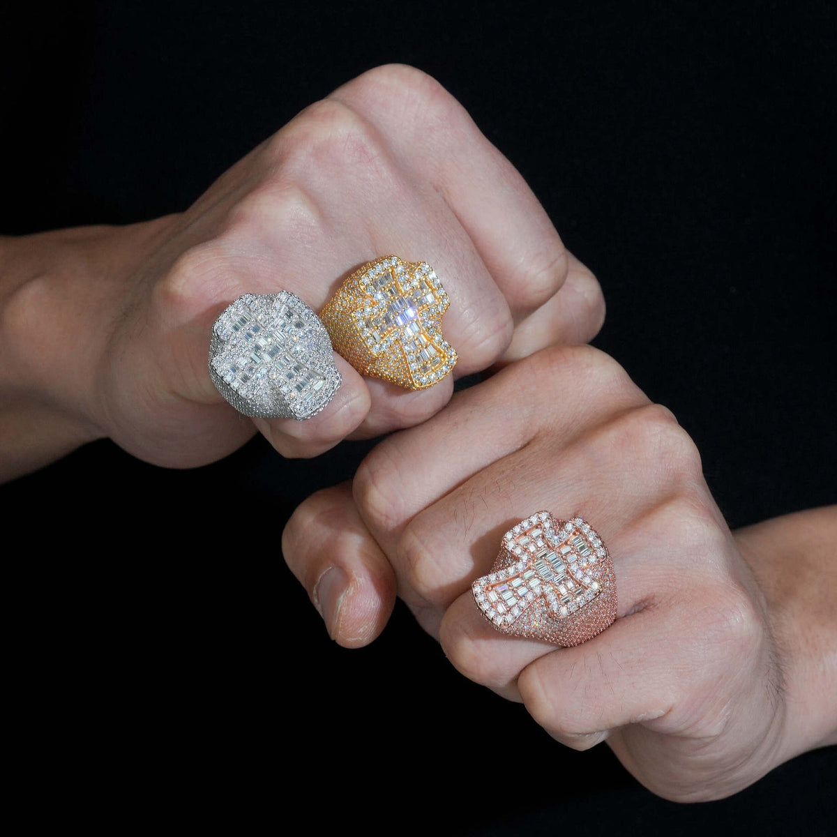 Person wearing iced out cross moissanite baguette statement rings in multiple gold finishes on hand