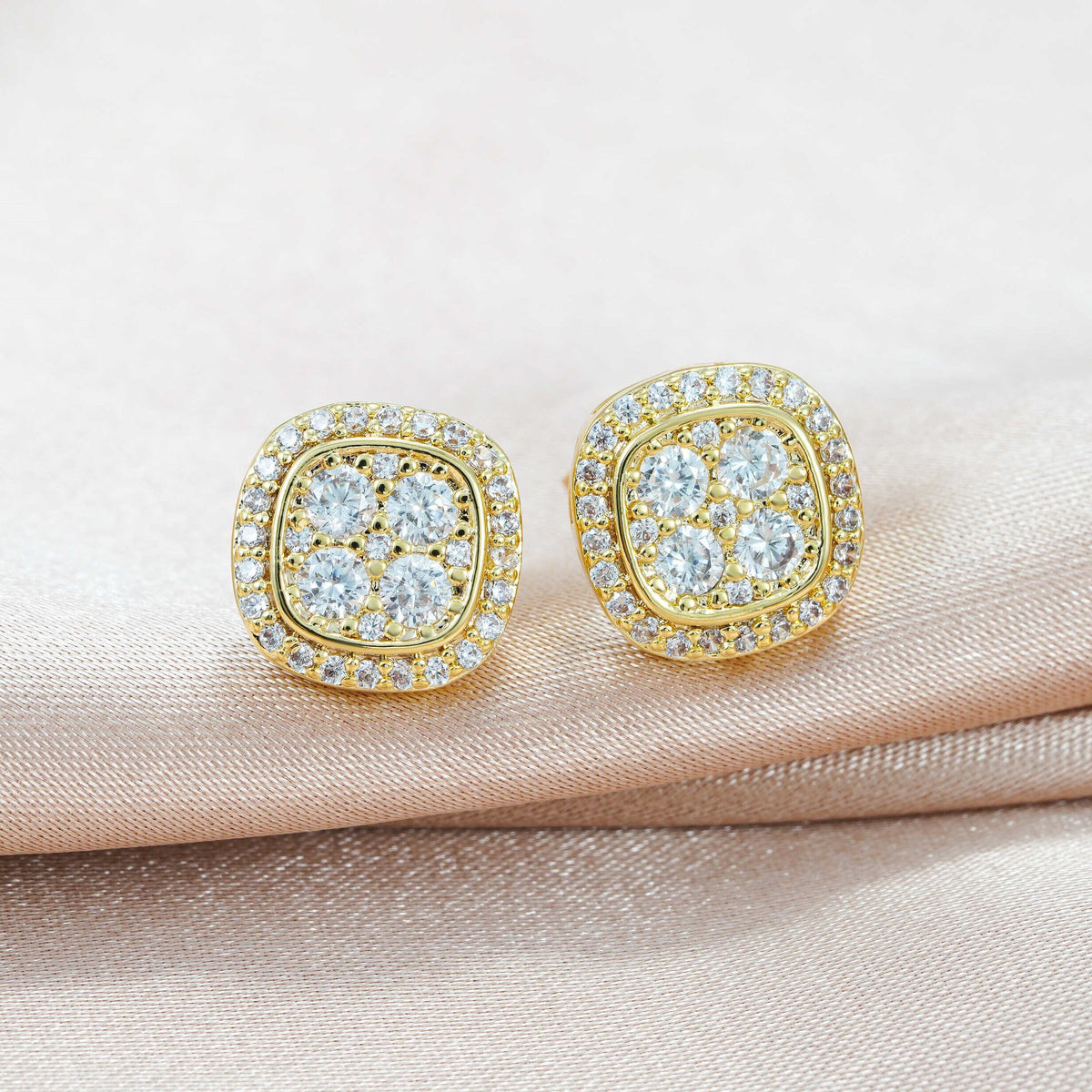 Pair of yellow gold iced out cushion square cluster moissanite stud earrings resting on satin ribbon surface