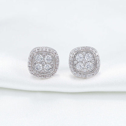 Pair of silver iced out cushion square cluster moissanite stud earrings on white silk cloth backdrop