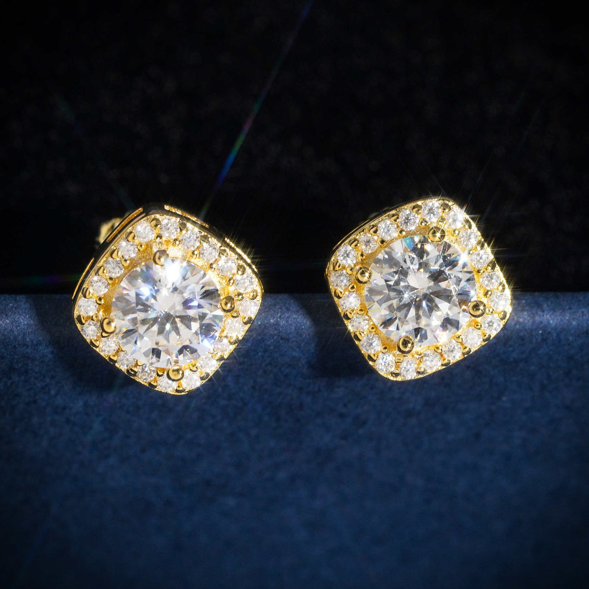 Pair of yellow gold iced out cushion square halo solitaire moissanite stud earrings on dark blue box