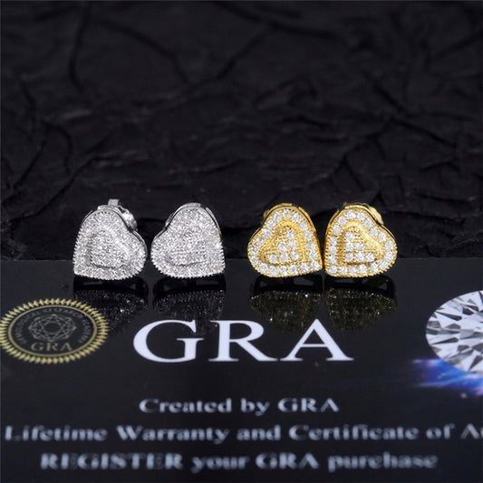 Three heart-shaped stud earrings displayed on a glossy black surface with a dark textured backdrop. Two earrings are silver-toned with clear stones, and one is gold-toned with clear stones.