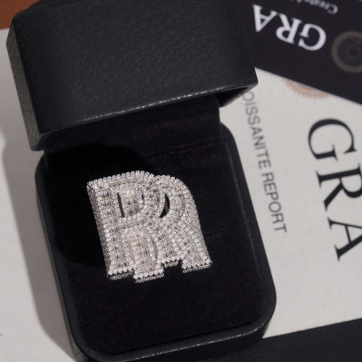 Iced out double letter RR moissanite ring displayed in black jewelry box with GRA certificate