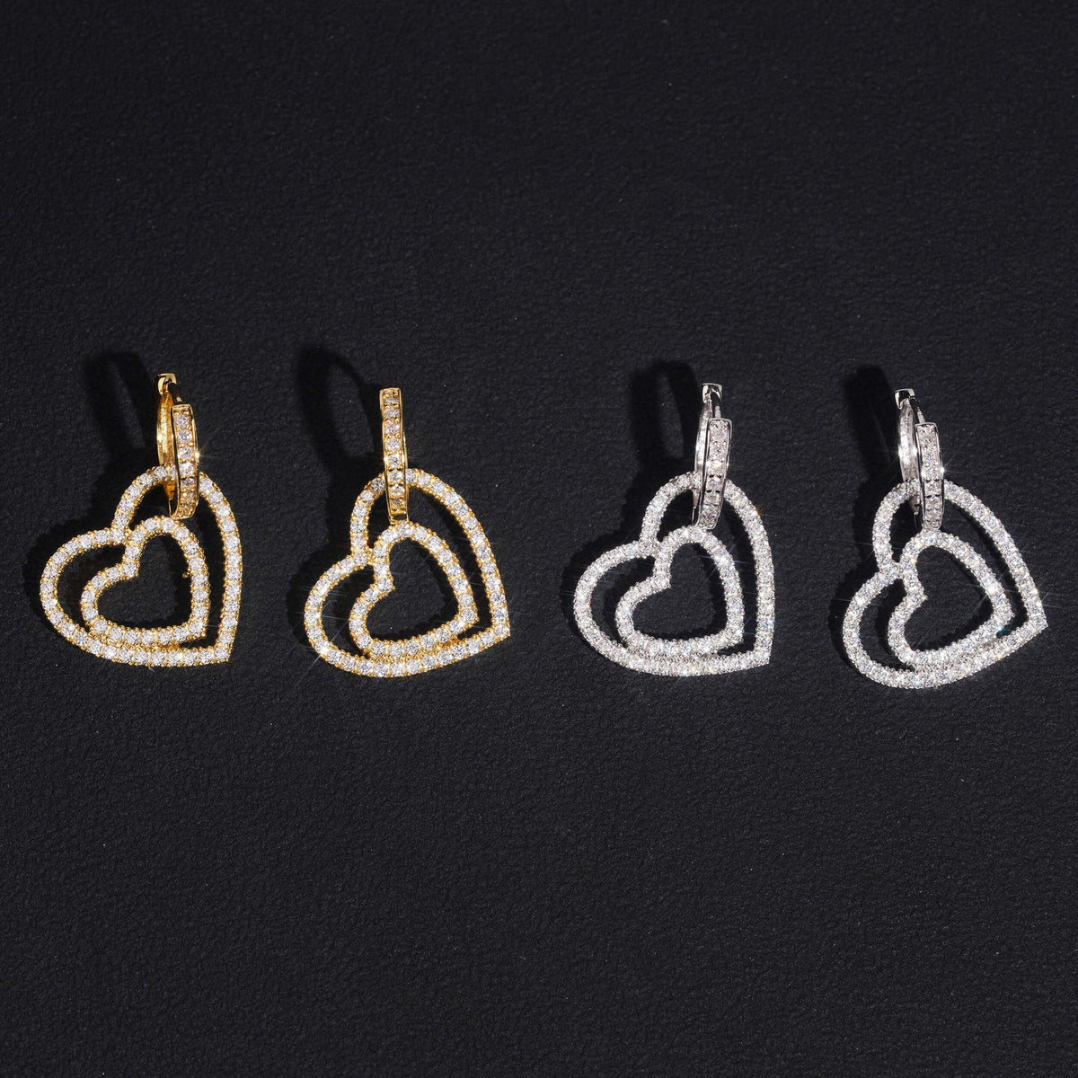 Iced out double open heart dangle huggie hoop moissanite earrings in gold and silver on black background