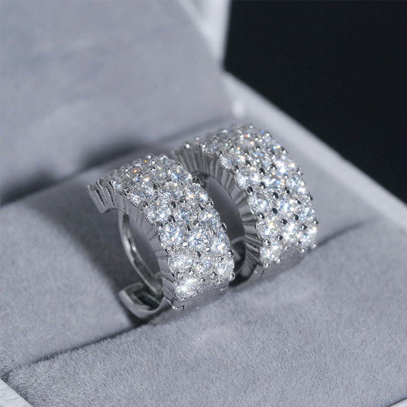 Pair of silver iced out double row pave moissanite huggie hoop earrings presented in velvet jewelry box