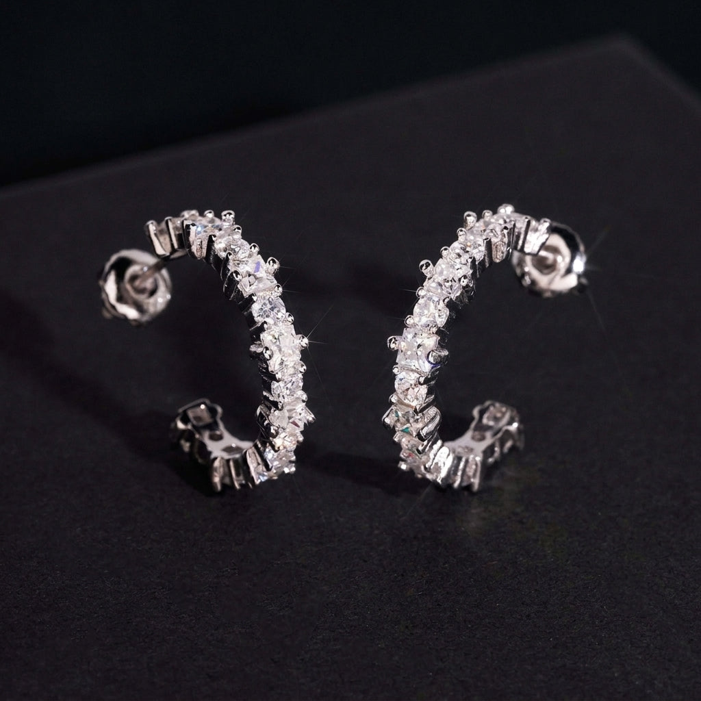Silver iced out eternity C-shaped half hoop moissanite stud earrings with pave setting on dark background