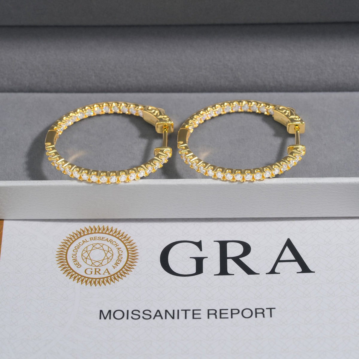 Yellow gold iced out eternity moissanite hoop earrings resting on velvet display box with GRA report card