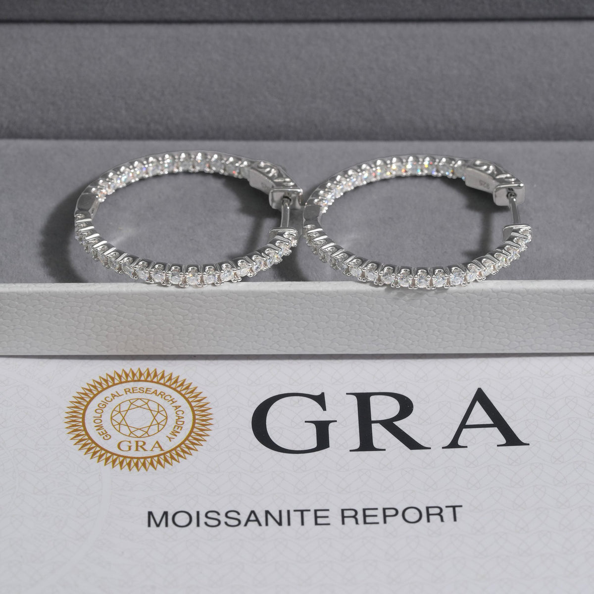 Pair of silver iced out eternity moissanite hoop earrings displayed on GRA report certificate card