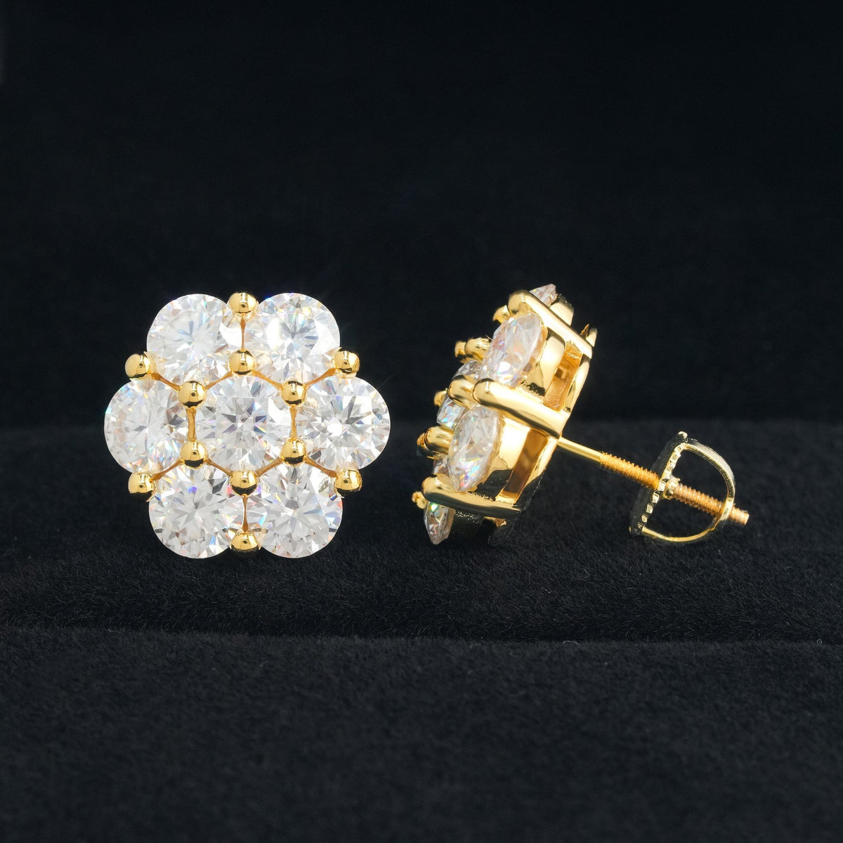 Gold, silver, and rose gold iced out flower 7-stone cluster moissanite stud earrings aligned on black display stand