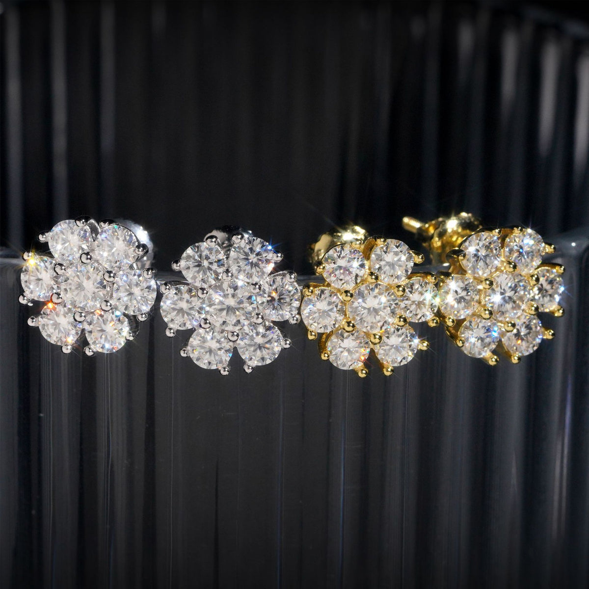 White and yellow gold iced out flower 7-stone cluster moissanite stud earrings aligned on black display stand